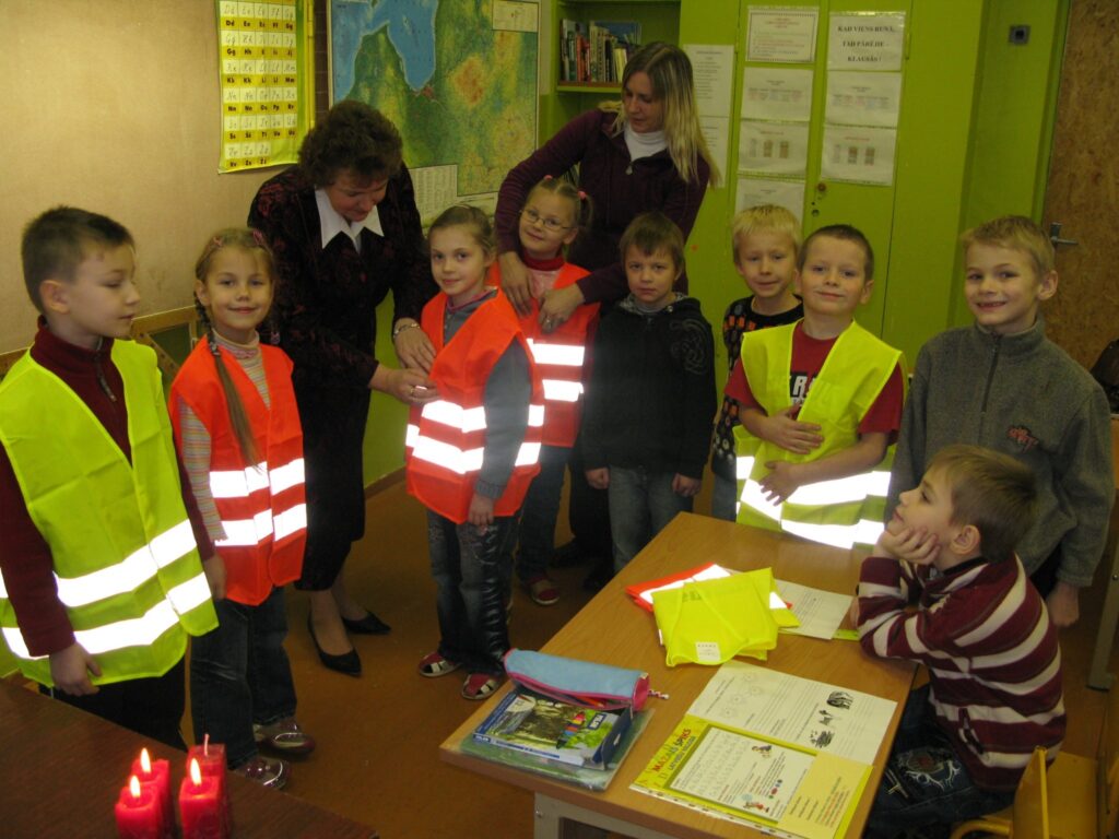  Palsmanes pamatskolas “pirmīši” kopā ar skolas direktori Daci Pērli (no kreisās) un  klases audzinātāju Santu Indrēvicu jau piemērījuši Īrijā dzīvojošā novadnieka Aivja Pitkēviča uzdāvinātās atstarojošās vestes. 
Autors: Sandra Pētersone