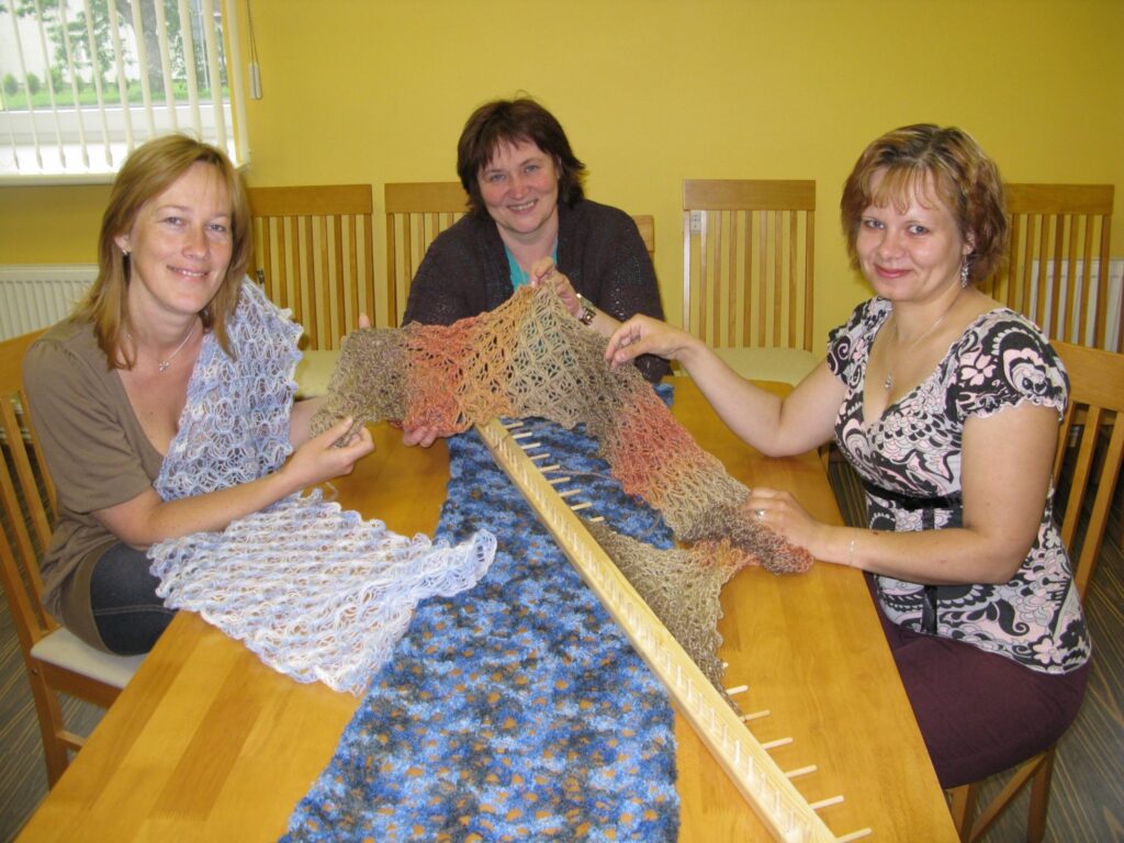 Palsmaniete Līga Treisnere (no labās) šalli tapo pati, bet Aijai Zeibotei (no kreisās) savu rokdarbu uzdāvinājusi Vingra Bērtiņa. Savukārt Birute Mežale priecājas par Dinas Ozolas šallīti, kas redzama priekšplānā uz galda. 
Autors: Sandra Pētersone