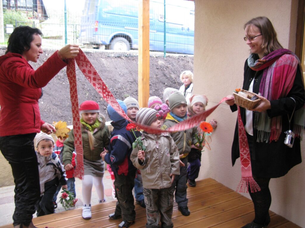 Atklājot rekonstruēto bērnudārza ēku Smiltenē, Mētras ielā, lenti negrieza, jo par goda vārtiem kalpoja skolotājas Ditas Baibas Brūzītes (no labās) austā Lielvārdes josta. 
Autors: Sandra Pētersone