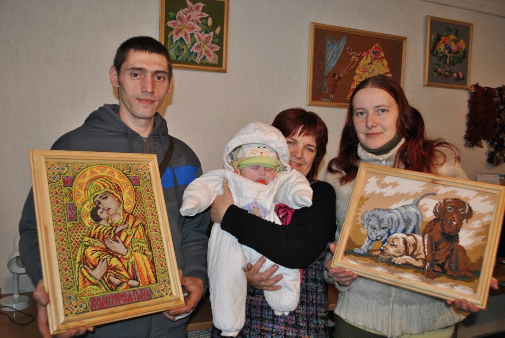 Smilteniešus Mārtiņu Zvaigzni un Inesi Zvirbuli parādīt  citiem savas krustdūrienā izšūtās gleznas uzaicināja kaimiņiene Maira Kupriša (vidū - attēlā ar Mārtiņa un Ineses meitiņu Lindu). Dievmātes gleznu Mārtiņš izšuva aptuveni trijos mēnešos. 
Autors: Sandra Pētersone