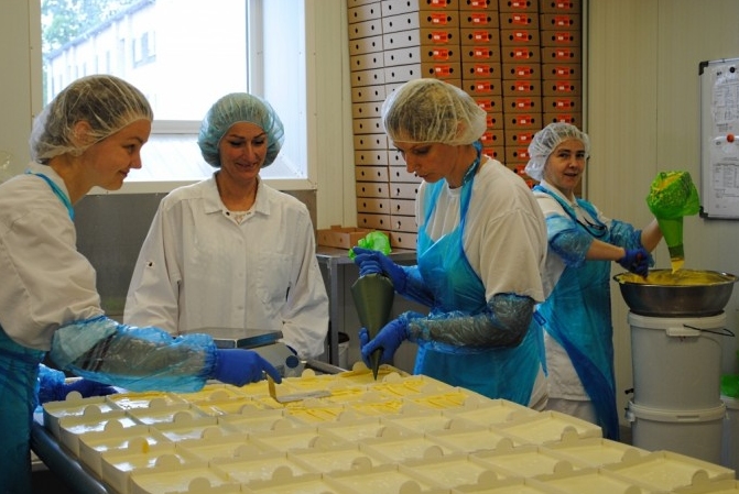 Top viens no jaunākajiem produktiem - Siera kūka Krēma kārtu klāj Līga Stīpniece (no labās), šokolādes garnējumu – Evija Lūse, procesam rūpīgi seko idejas autore Agita Opmane un procesā noder arī palīgi, kas šeit strādā Nodarbinādības valsts aģentūras projekta ietvaros. 
Autors: Sarmīte Ozola