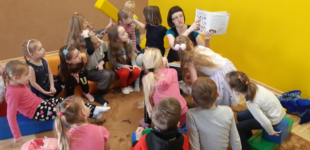 Bērni sasēžas aplī, un Bērnu literatūras nodaļas bibliotekāre Una Grāve lasa grāmatas un iesaista viņus uzdevumos.                                    
Autors:  LĪGA ORLEANA