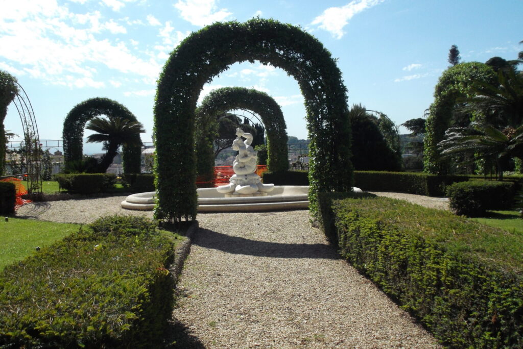 Celiņi no dažādiem dārza stūriem ved mūs pakalnā. Ejam caur vīteņaugu zaļajām arkām kā godavārtiem, lai tur kalnā ieraudzītu Vatikāna lepnumu – rožu dārzu.