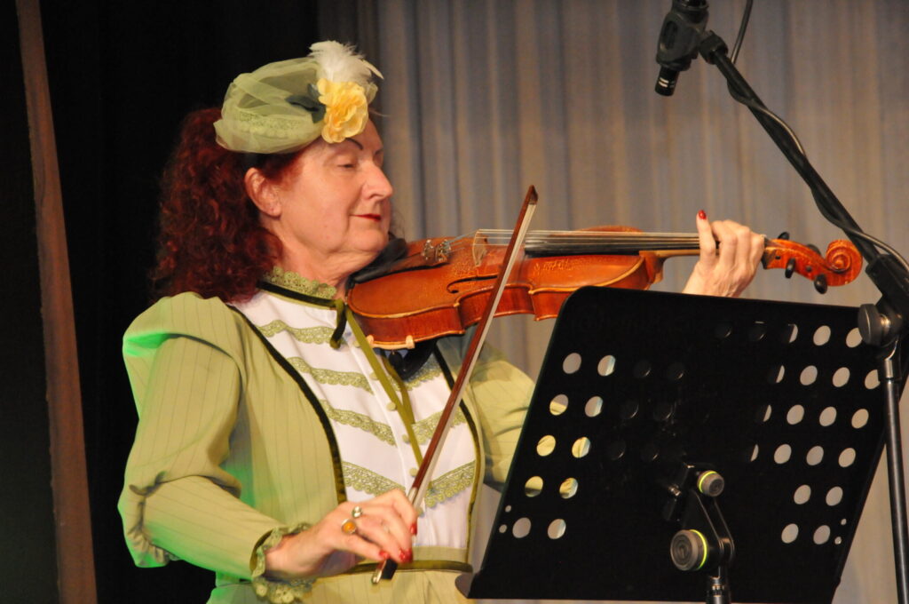 Vijolniece Līga Veinberga, tērpusies gaumīgā koncerttērpā, muzicē kopā ar savējiem no tautas mūzikas kapelas “Sudmaliņas”.
