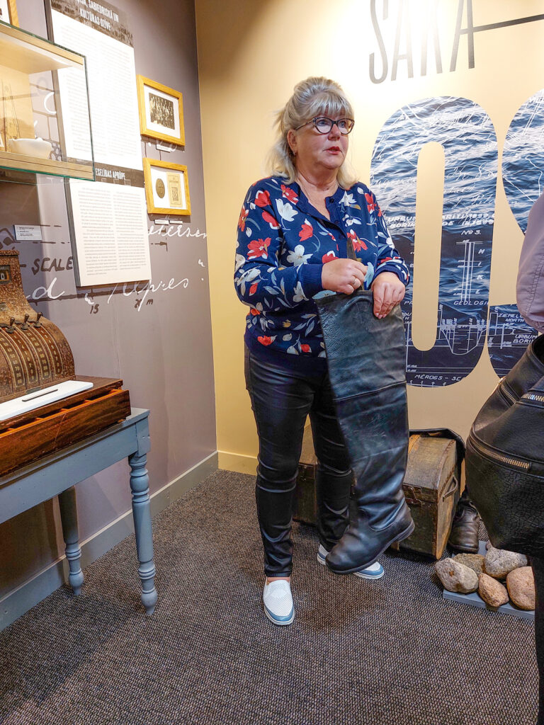 Vietējā gide rāda garu un smagu 30. gadu zvejnieka zābaku no teļādas.